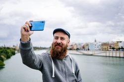 Satisfied male tourist taking selfie on smartphone at quay