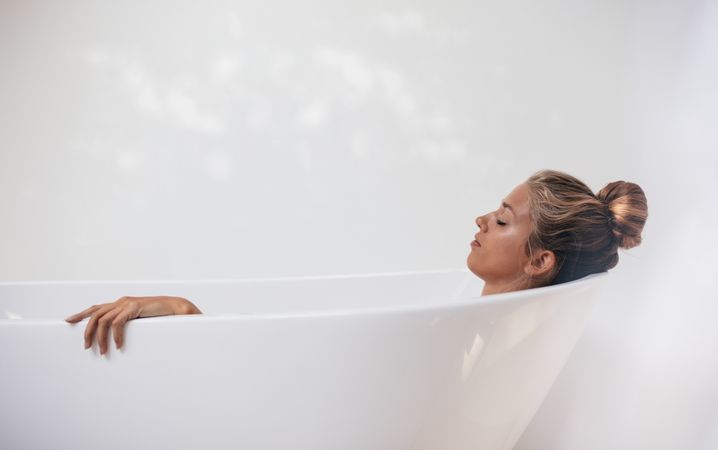 Side view shot of young woman lying in bathtub with her eyes closed