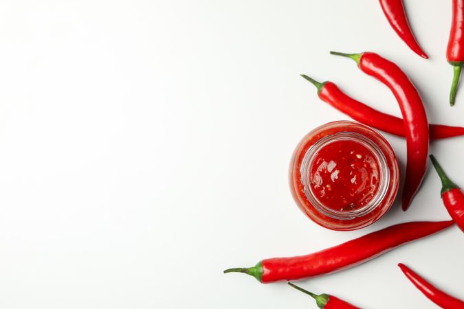 Glass jar with sauce and chilli pepper on blank background, top view