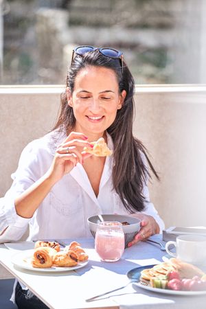 Positive woman eating delicious croissant for breakfast in sunny