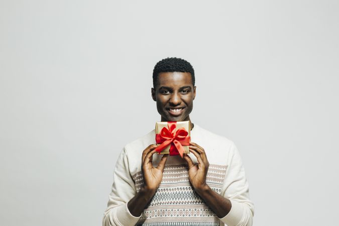 Happy Black man holding gold box with red bow below his face
