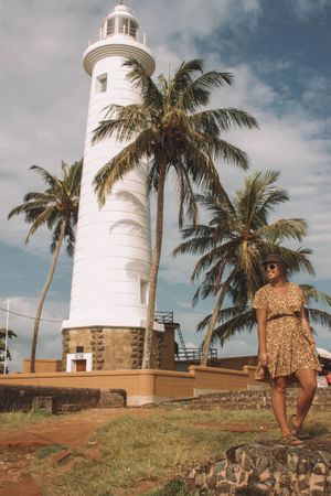 Woman in brown floral dress standing beside lighthouse