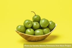 Green olives in eco friendly wooden bowl isolated on yellow background 5rxn3b