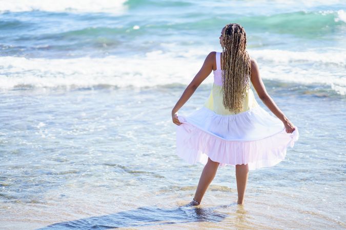 Barefoot Black woman walking in the water at beach in colorful dress