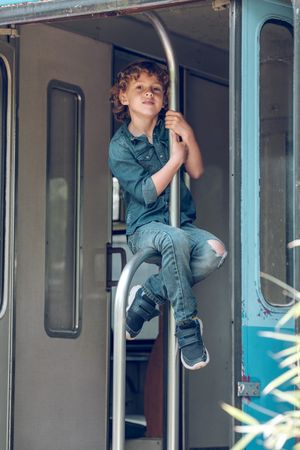 Preteen boy sitting on metal handrail of train