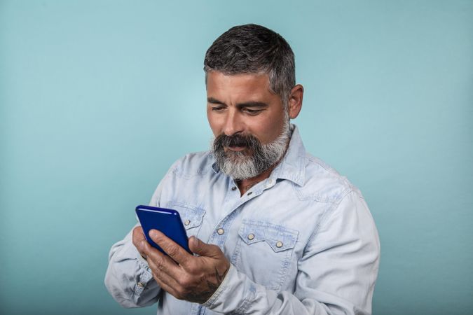Smiling middle aged man using smartphone standing against blue background