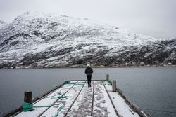 Woman on waterfront against small town at snowy foothill