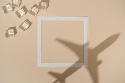 Shadow of airplane over beige paper background with square and ice cubes