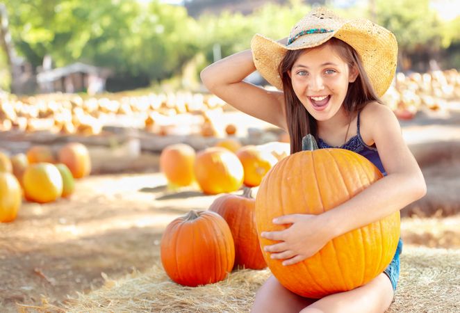 Girl Wearing Cowboy Hat Enjoying The Pumpkin Patch on a Sunny Fall Day.