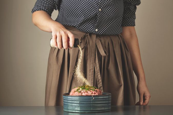 Woman shaking spice mixture onto ground meat
