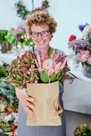 Happy female florist with bouquet of flowers in paper bag