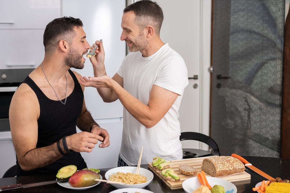Male couple tasting pasta as they prepare meal