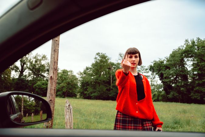 Woman in red sweater gesturing near car on road