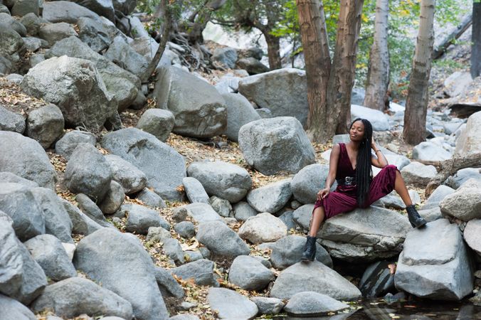 Woman sitting on boulders with her eyes closed and hand on her neck