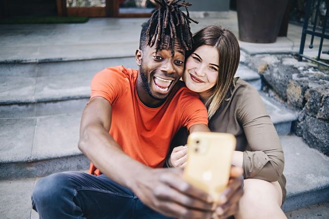 Interracial couple taking selfie on steps outside