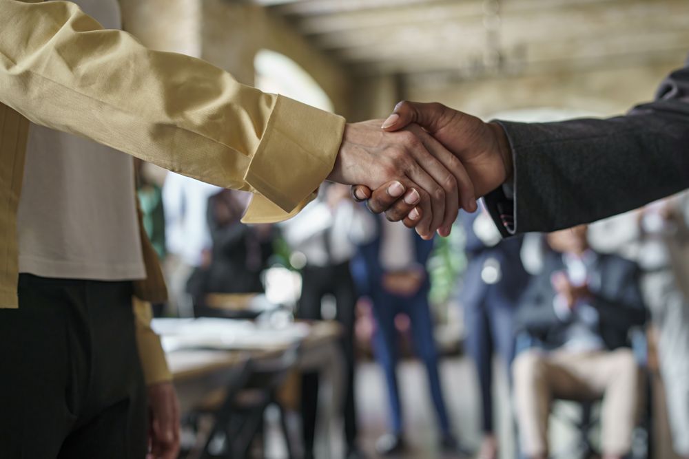 Multi-ethnic businesswoman shaking hands with blurred colleagues in the background
