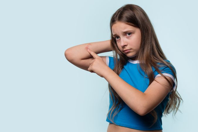 Young girl pointing at a cut on elbow, looking worried