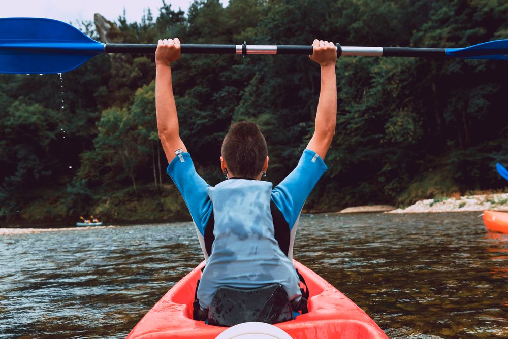 Female kayaking with paddle in raised hands