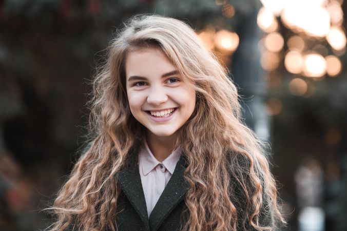 Smiling teenage girl in dark coat standing outdoor