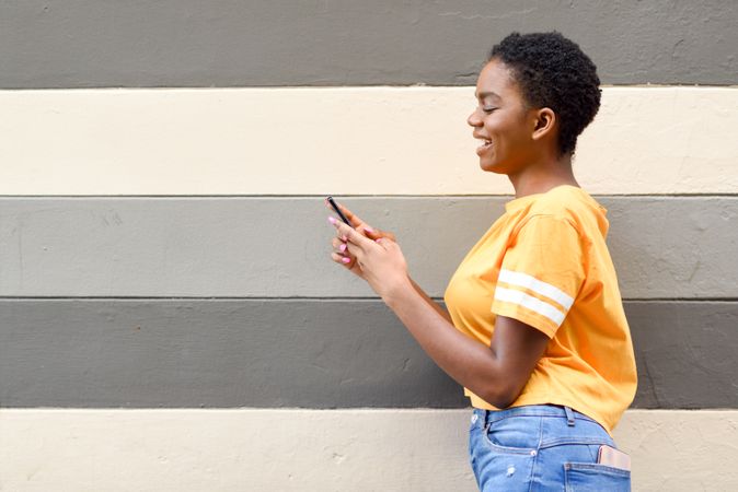 Smiling female checking phone in front of striped wall