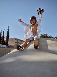 Excited boy with skateboard sitting on ramp