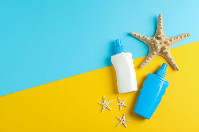 Flat lay composition with sunscreen sprays and starfishes on two tone background, space for text. Summer vacation backdrop