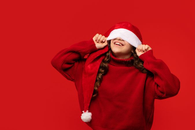 Girl playfully pulling Santa hat over eyes while smiling.