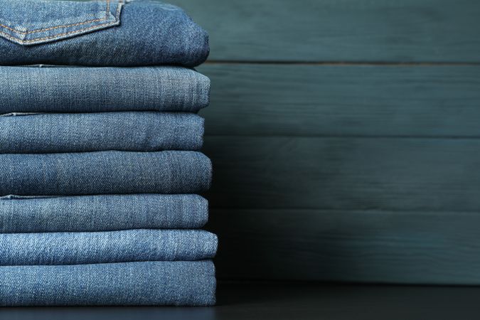 Stack of jeans pants on table, space for text