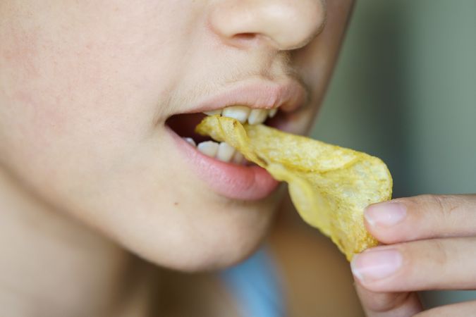 Crop anonymous girl biting crunchy potato chip