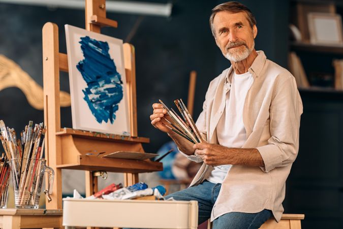 Male artist sitting in front of easel with his paint brushes