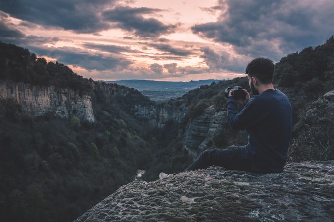 man with photo camera sitting on hill mountain with magnificent sunset