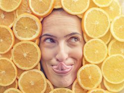 Funny woman licking nose among slices of oranges