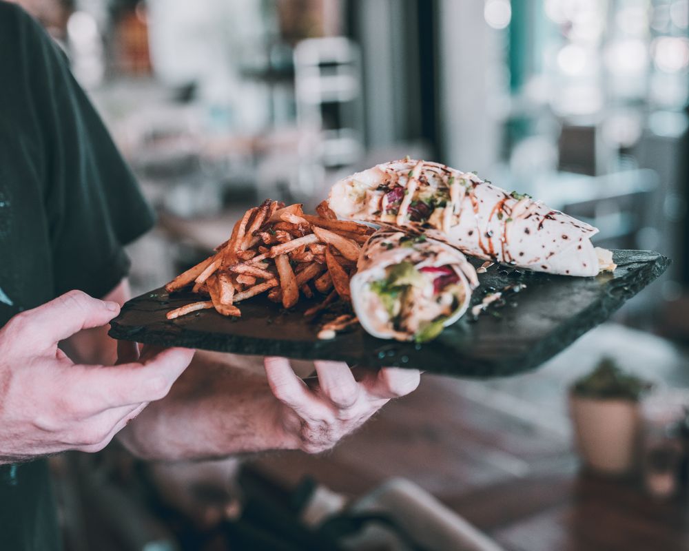 Cropped image of waiter holding a plate of wrap with fries