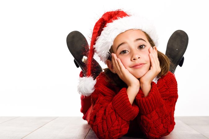 Child in santa outfit relaxing on stomach on ground resting her head on her hands