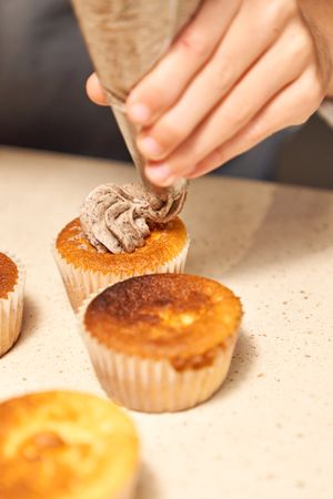 Crop person decorating cupcakes with cream