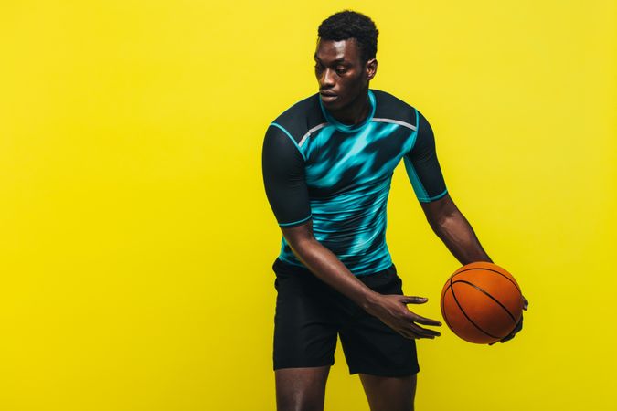 Black man playing basketball on yellow background