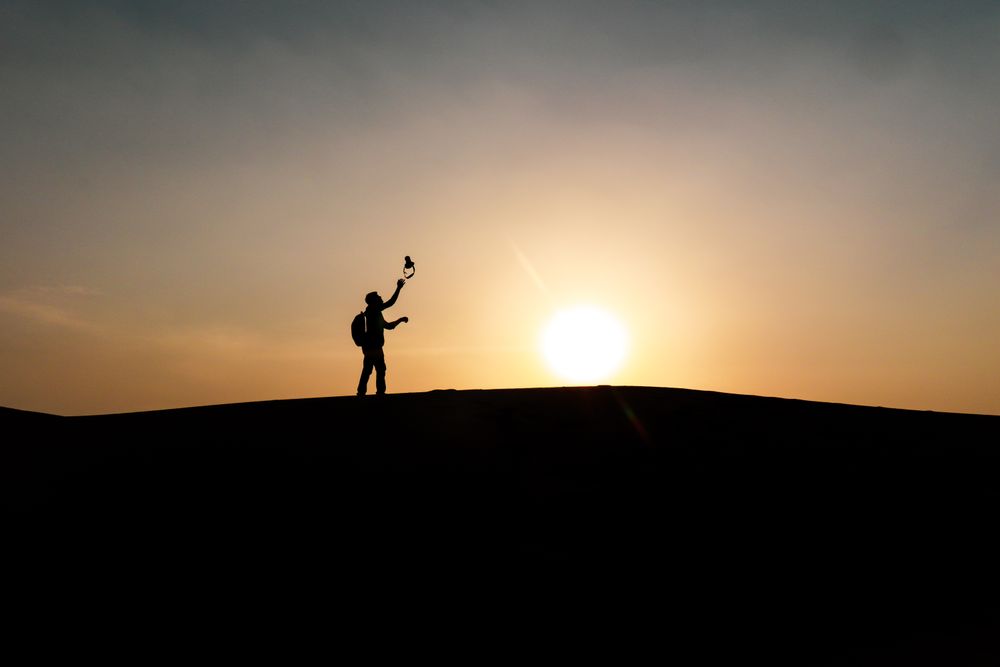 Silhouette of person with backpack on hill during sunset