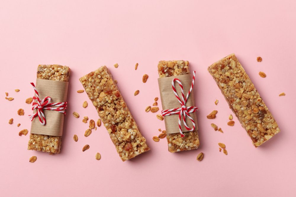 Tasty granola bars on pink background, top view