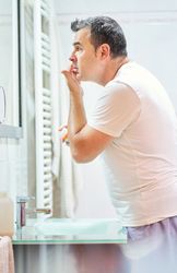 Man touching face in bathroom while looking in mirror