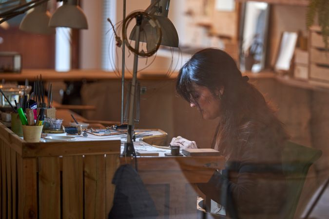 Attentive female goldsmith working with various tools in