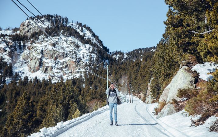 Man with smartphone between hills with trees in winter