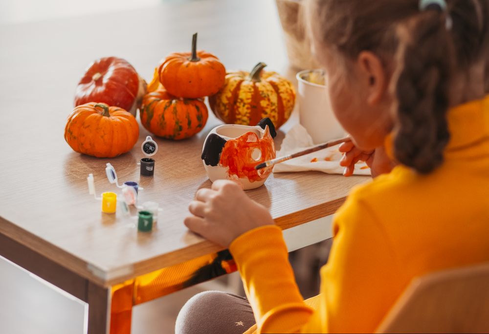 A little girl paints a clay hand made pumpkin. Halloween party. Crafts for children.