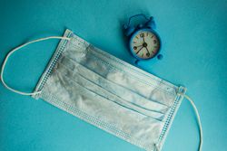 Clock and facemask on blue pastel background