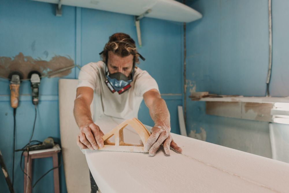 Man in respirator polishing surf board in workshop