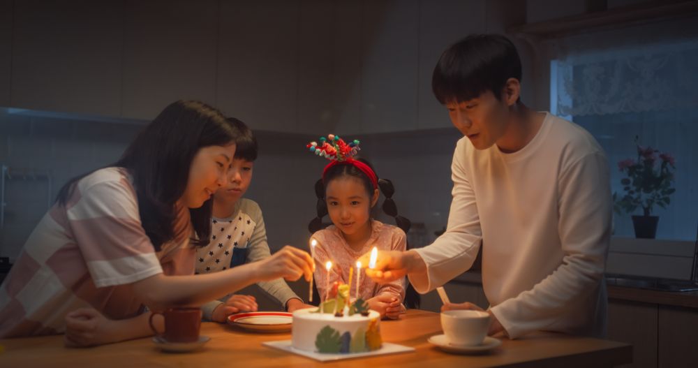 Cute Korean Family Celebrating a Birthday with Cake and Candles at Home During Evening.