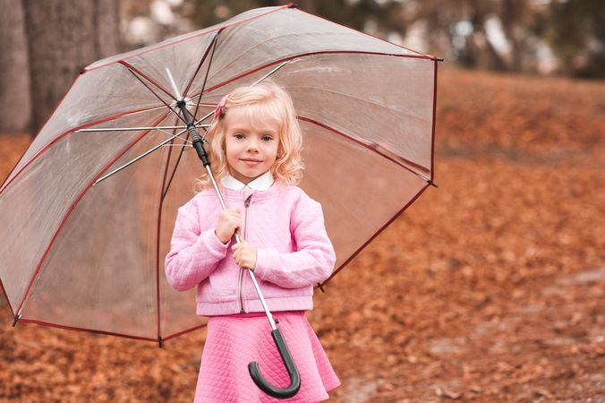 Girl in pink outfit holding an umbrella standing on autumn tree leaf