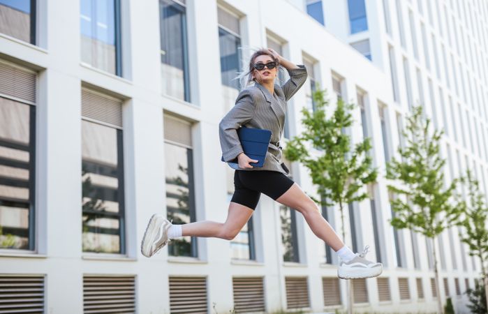 Woman with tablet in stylish suit jumping holding sunglasses