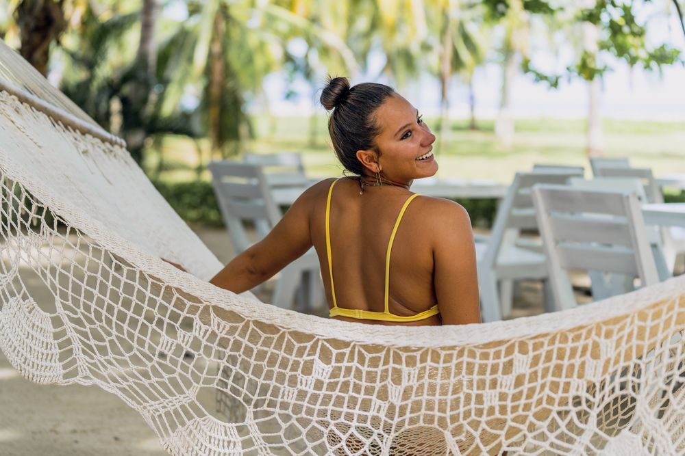 Joyful woman in bikini resting in hummock on beach