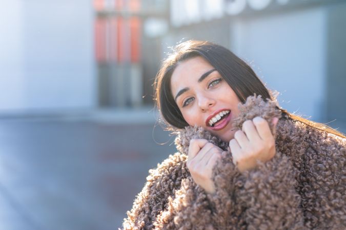 Cheerful woman wrapping in coat on street