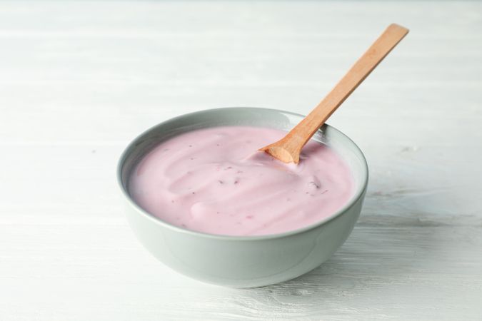 Fruit yogurt in bowl and spoon on wooden background